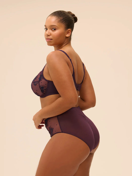 Woman wearing a dark purple lingerie set on a beige background