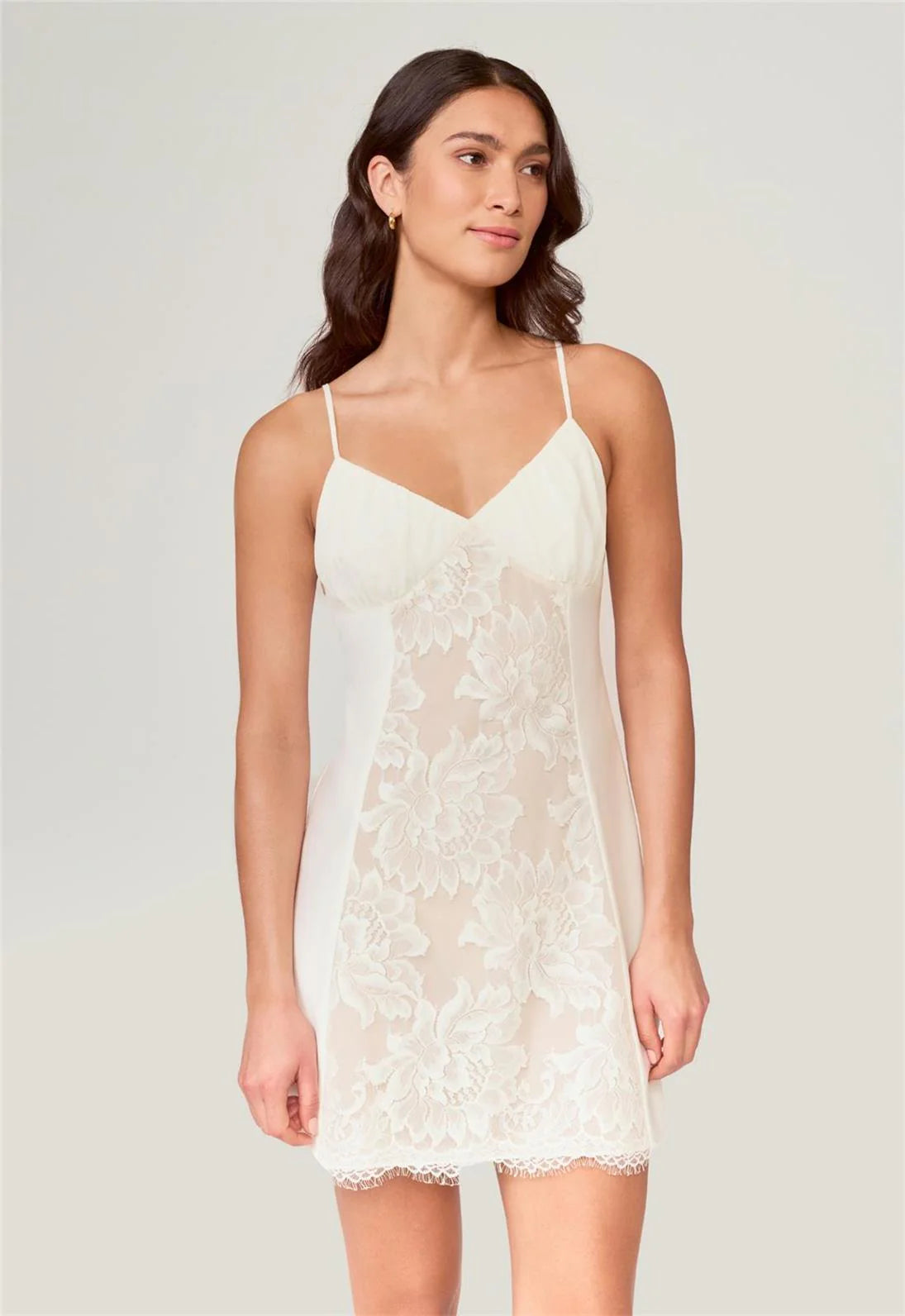 Woman wearing a white lace slip dress against a plain background