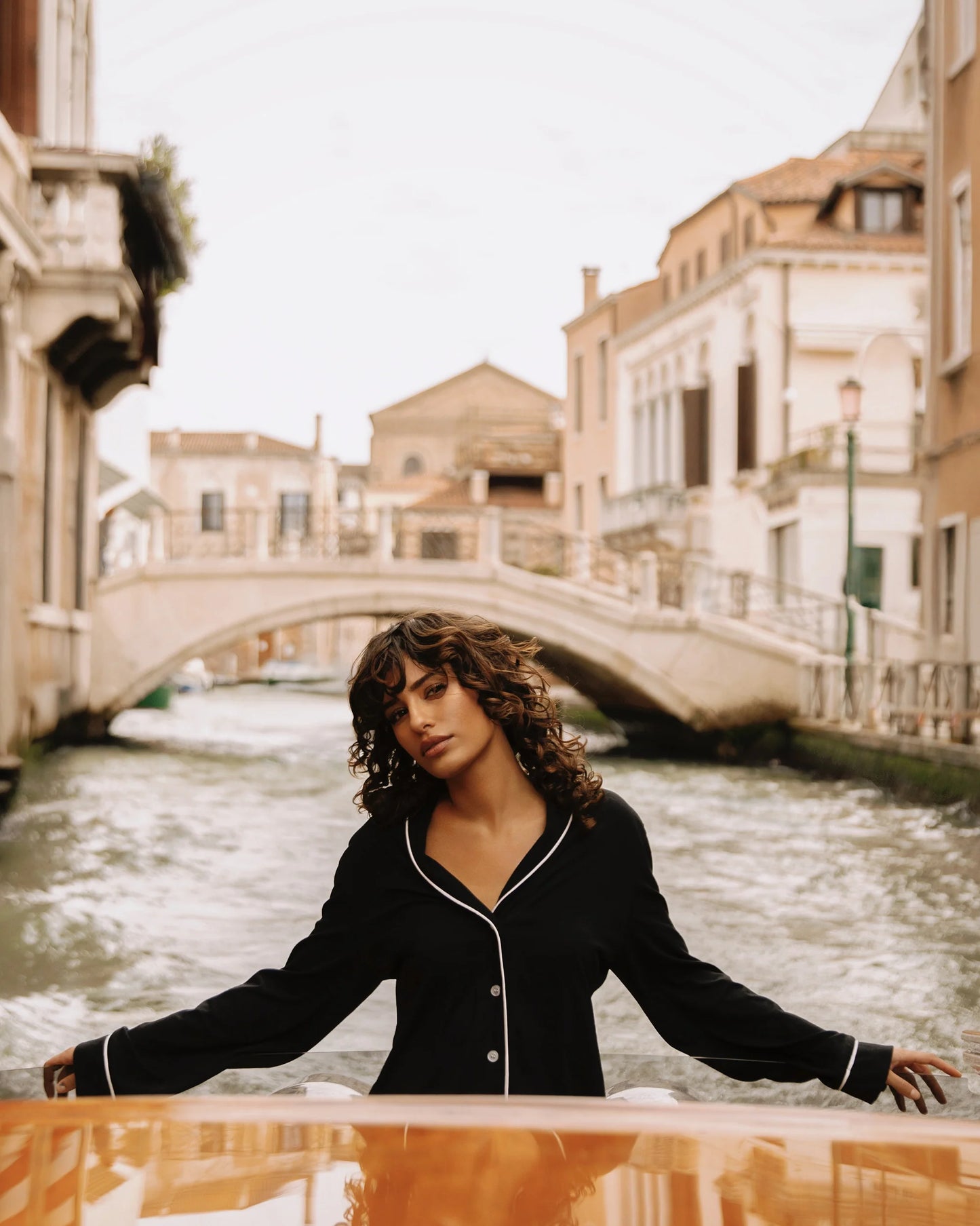 Woman standing by a canal with a bridge and buildings in the background