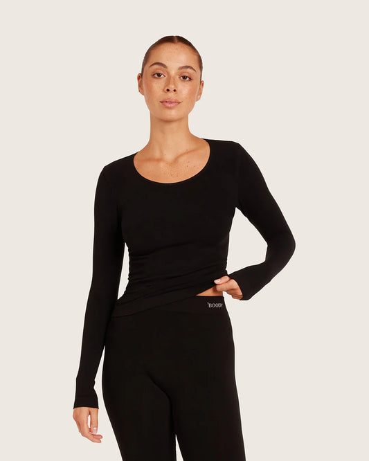 Woman wearing a black long-sleeve top and black leggings on a light gray background