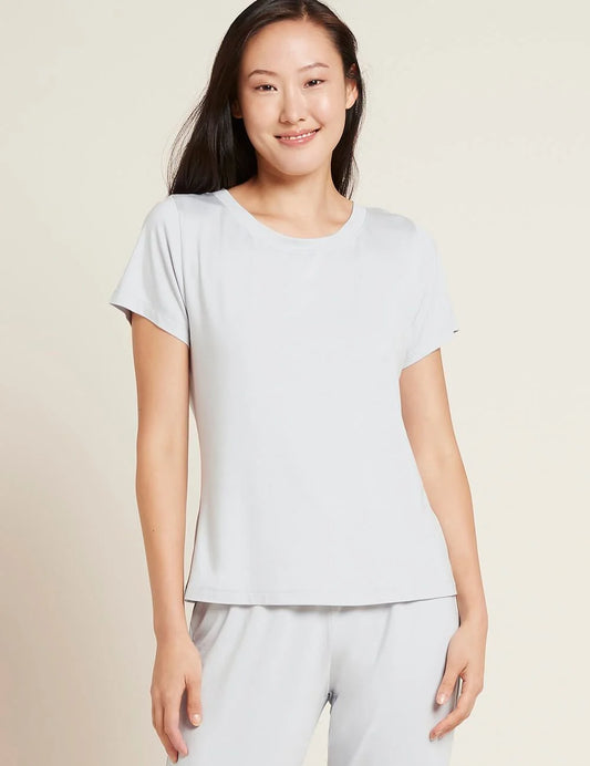 A woman modeling a light gray short-sleeve crewneck t-shirt and matching light gray pants against a solid beige background.