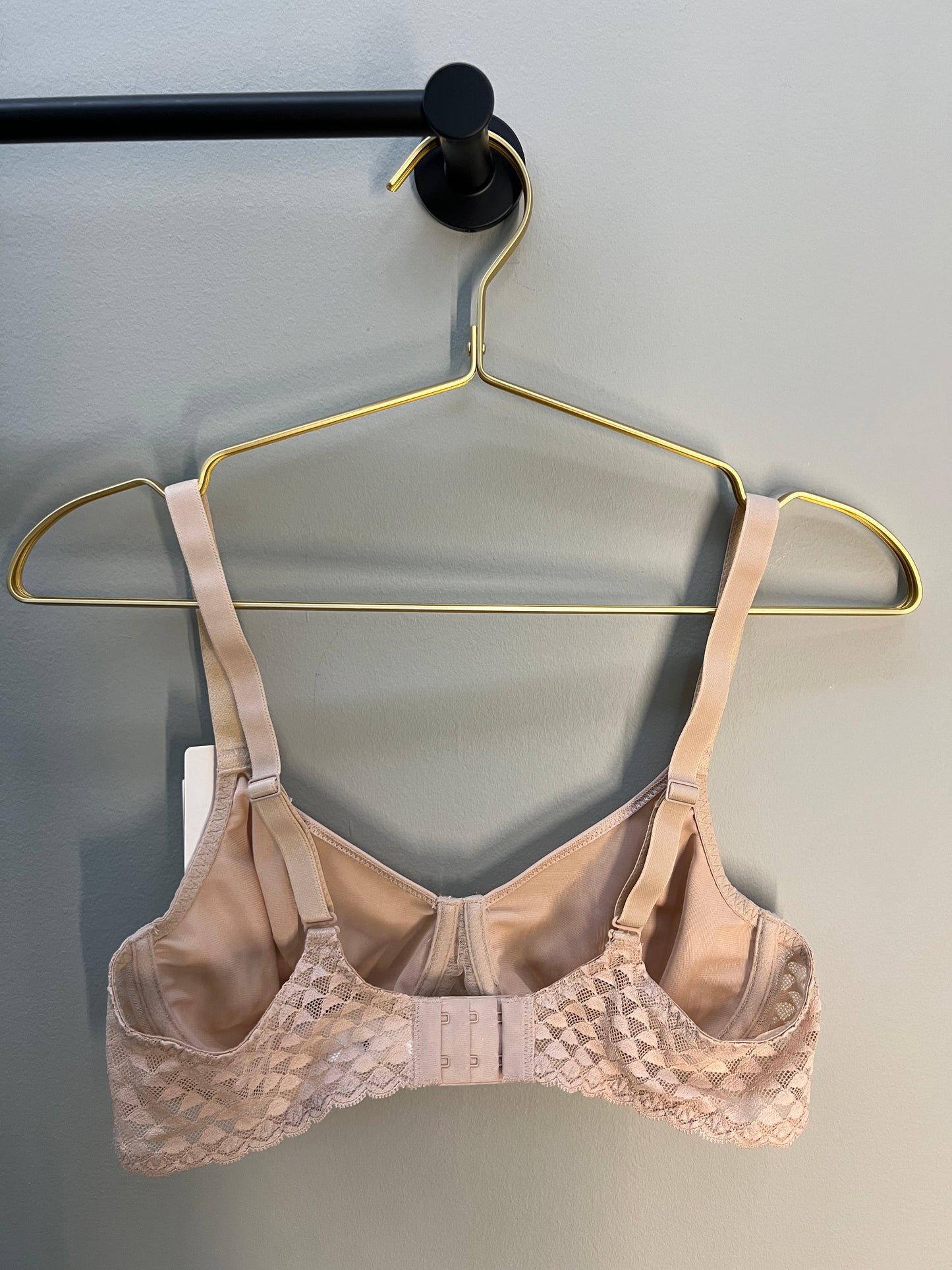 Beige bra on a gold hanger against a gray background