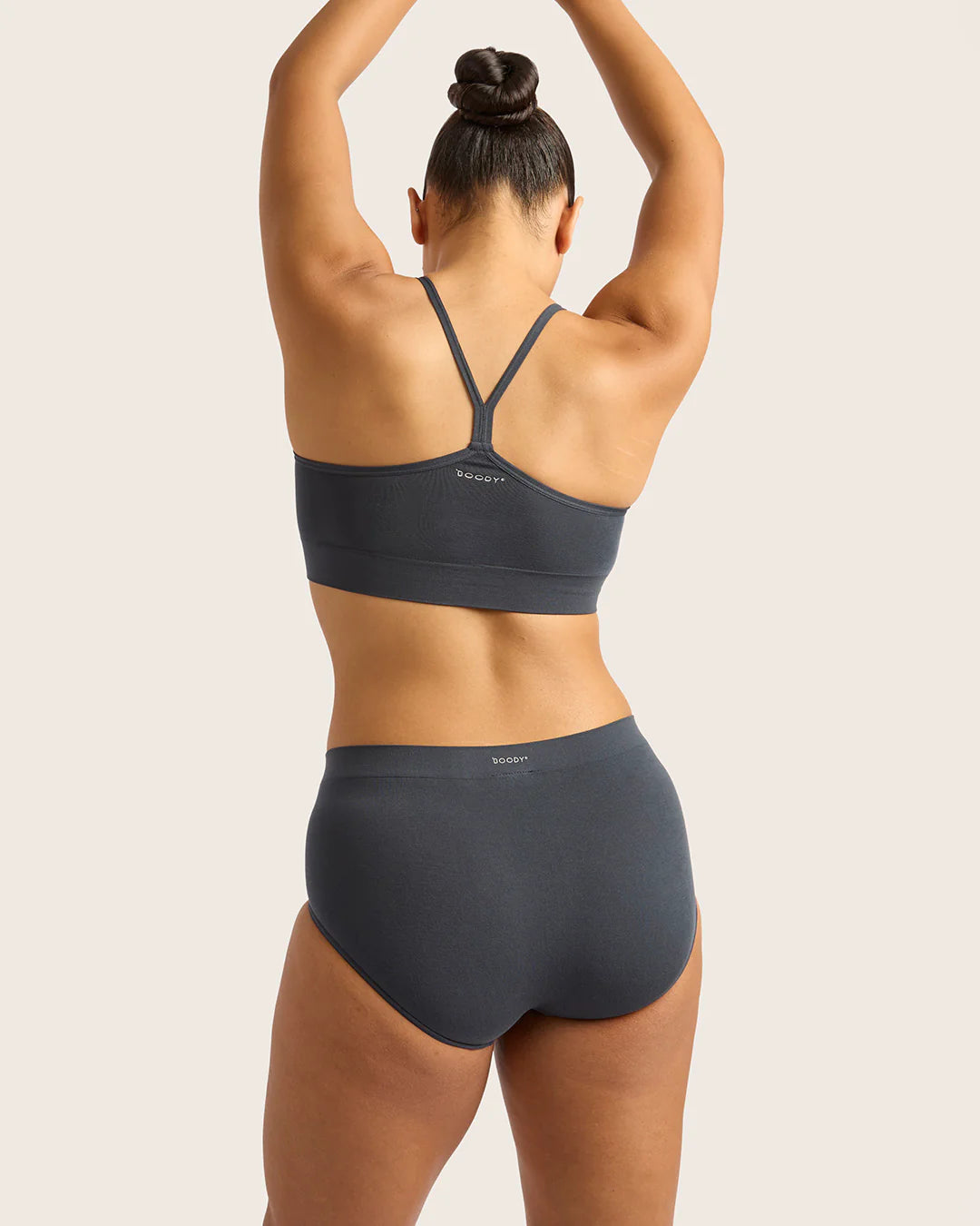 Person wearing a dark gray sports bra and high-waisted underwear set on a light background