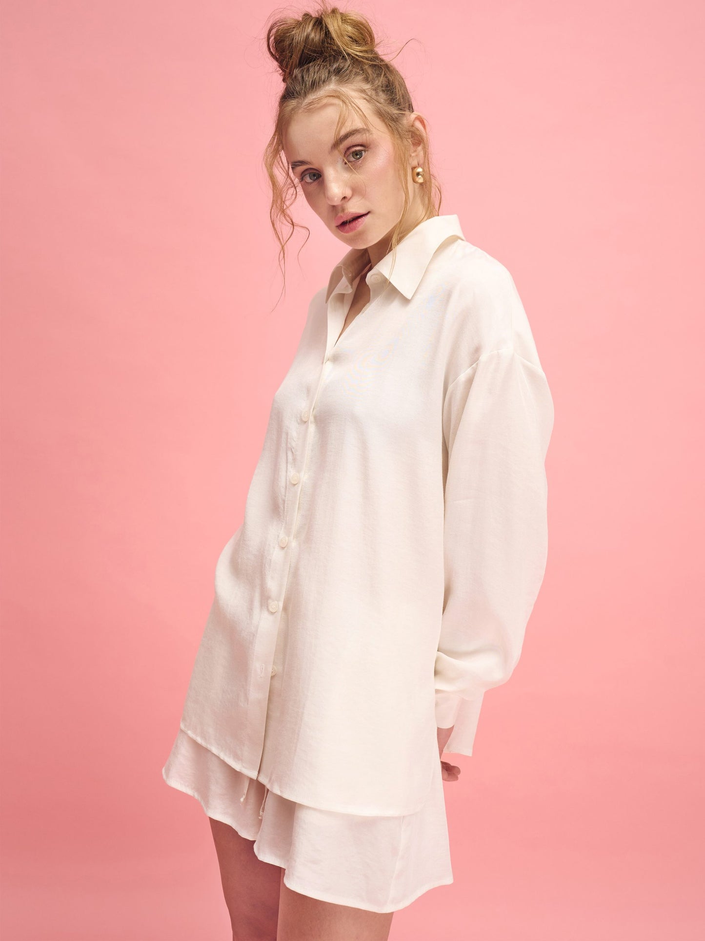 Woman wearing a white shirt dress against a pink background