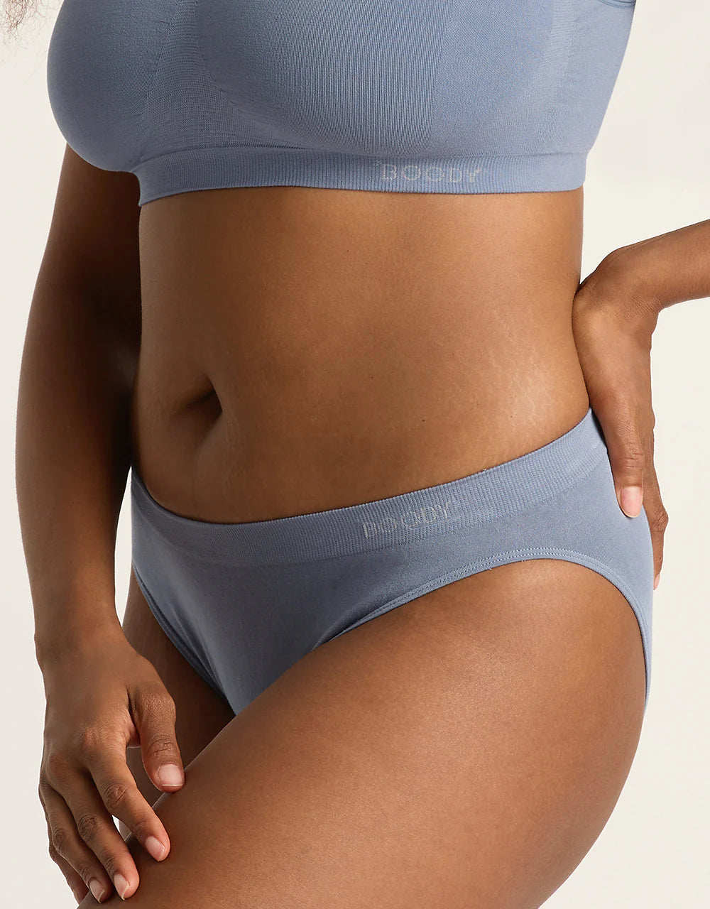 Person wearing a blue bra and underwear set on a neutral background