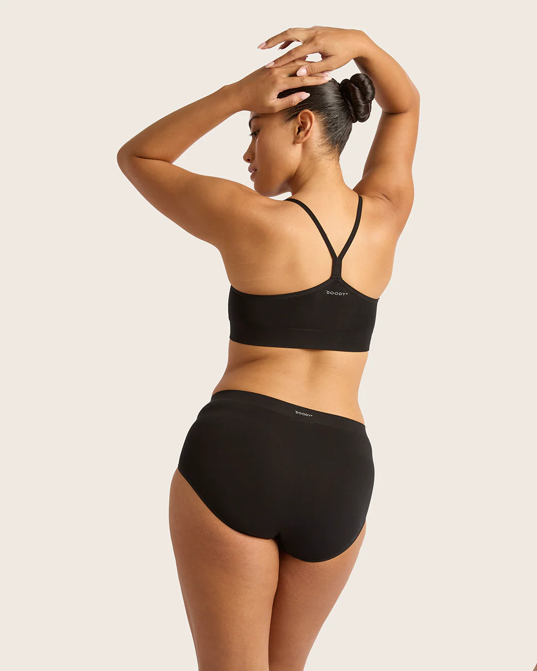 Woman wearing a black sports bra and high-waisted underwear set on a beige background