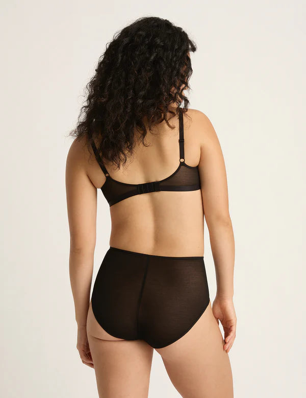Woman wearing a black bra and panties set on a beige background