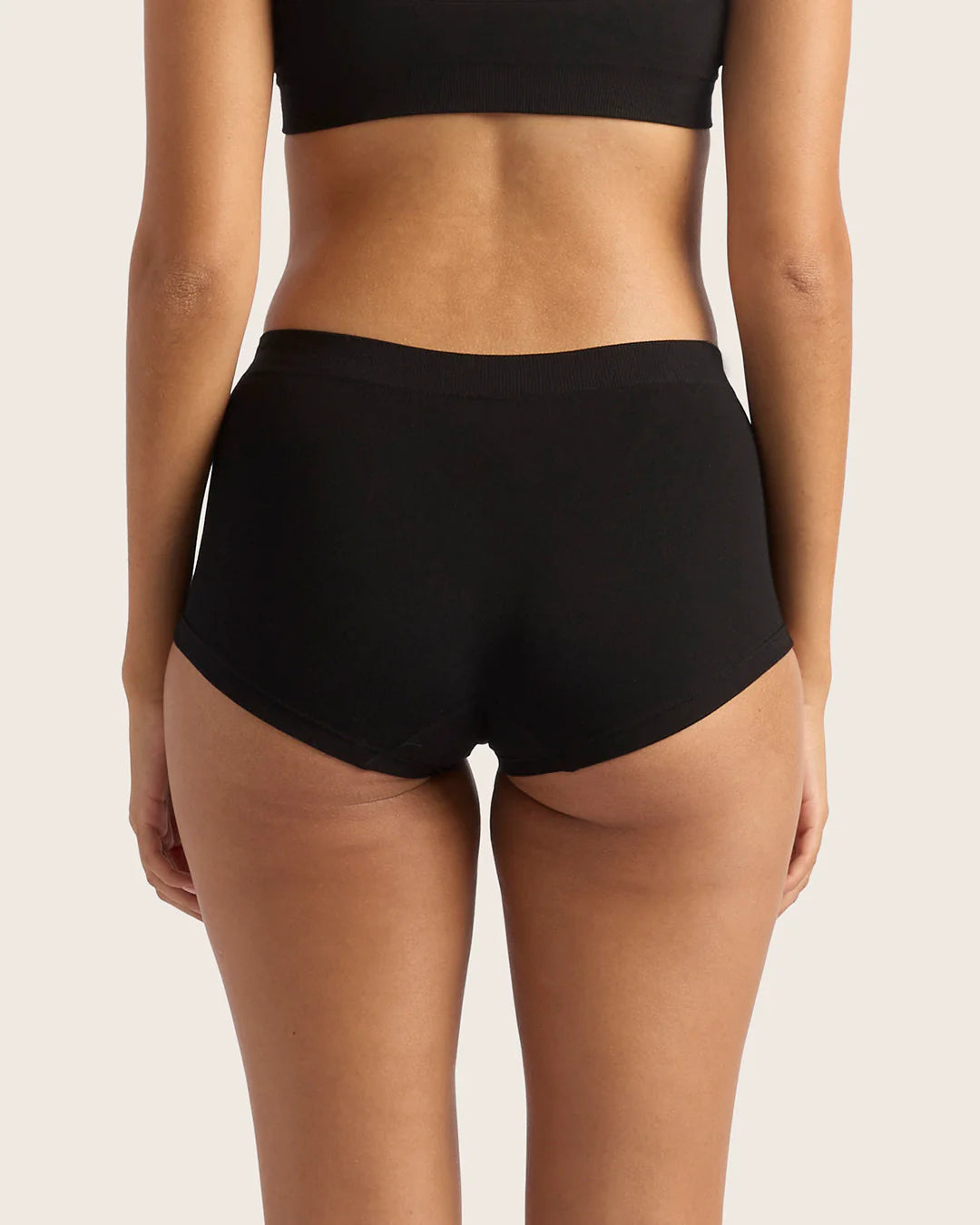 Person wearing black high-waisted bikini bottoms on a light pink background
