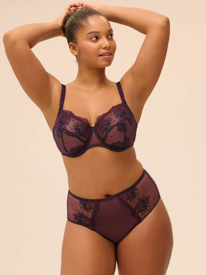Woman wearing a dark purple lace lingerie set against a beige background