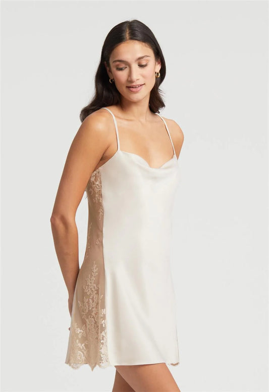 Woman wearing a white slip dress with lace details on a plain background