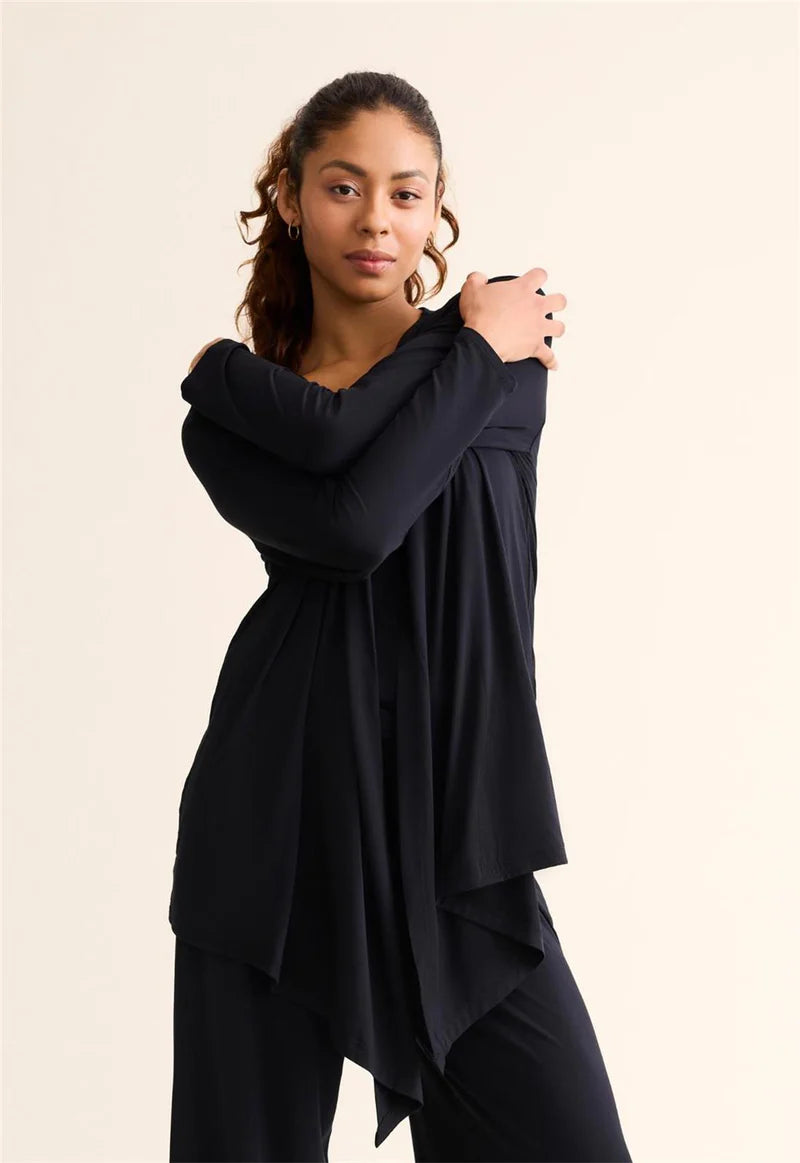 Woman wearing a black outfit with a flowing design against a beige background