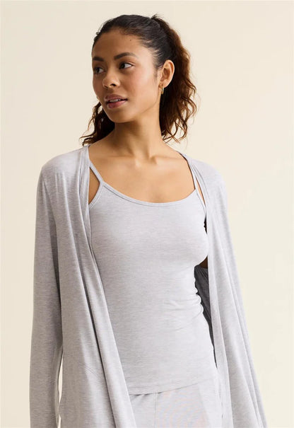 Woman wearing a light gray cardigan over a white top against a beige background