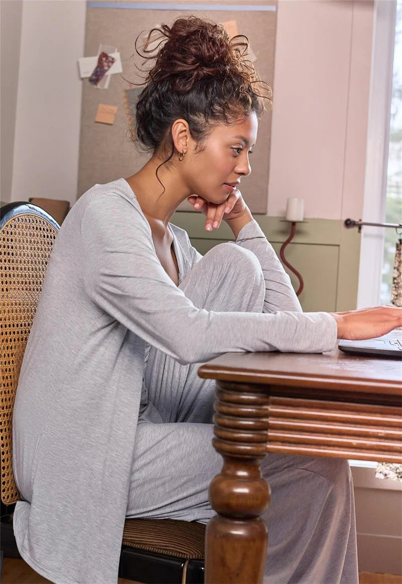 Woman sitting at a wooden table in a home setting, looking at a laptop.