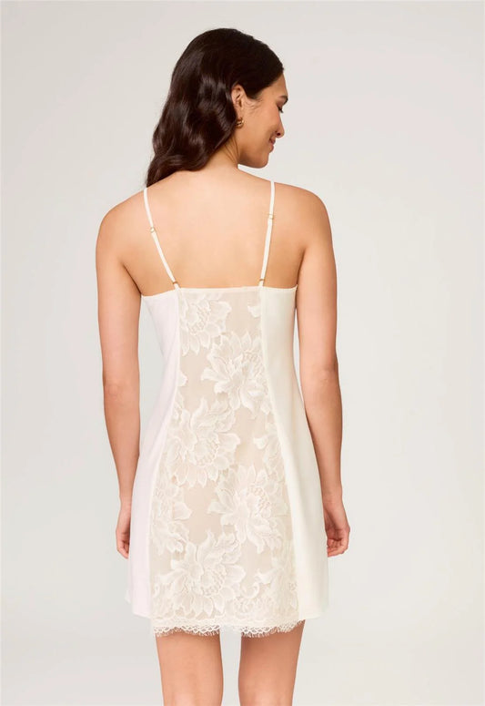 Woman wearing a white lace slip dress against a plain background