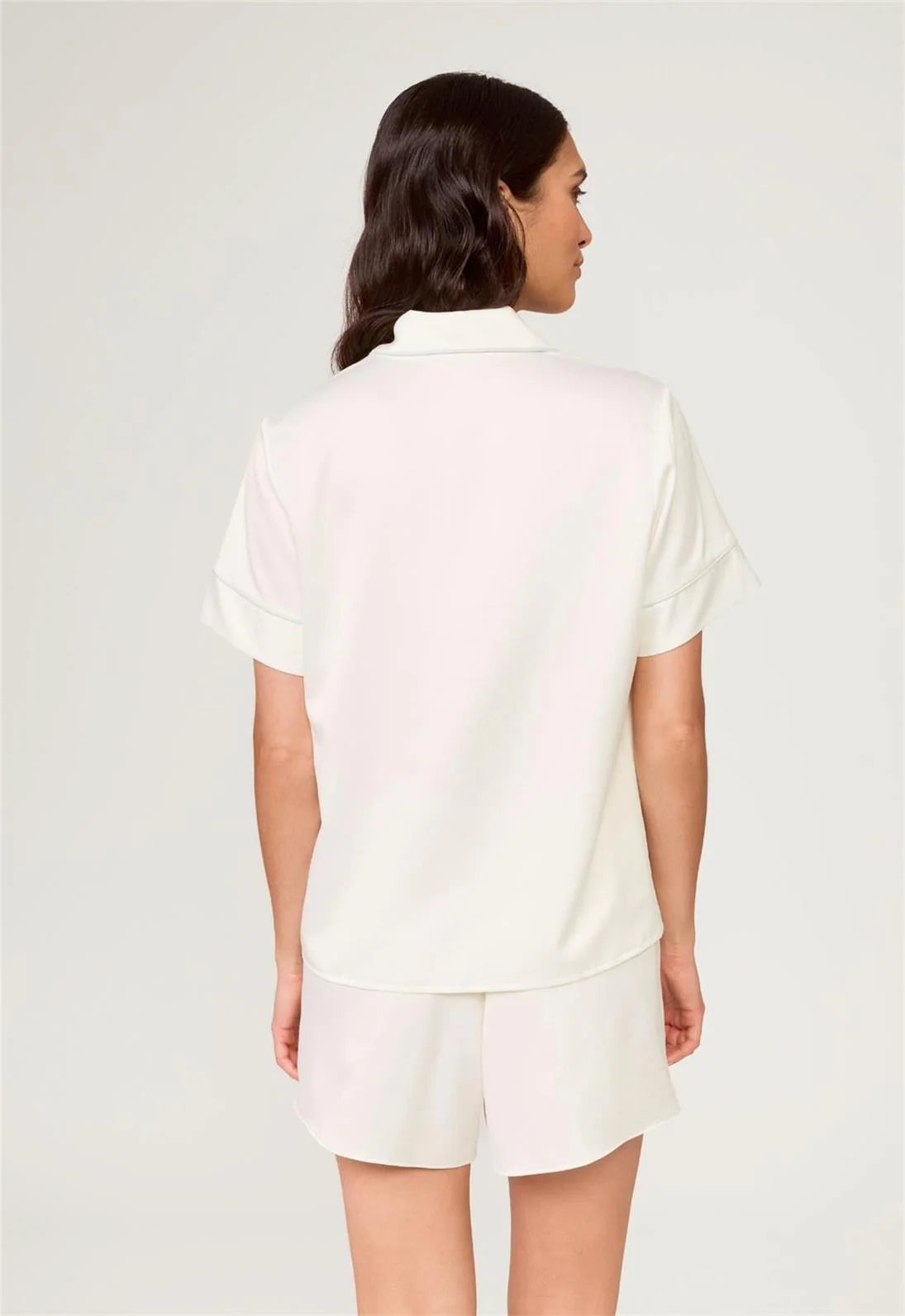 Woman wearing a white polo shirt and shorts on a light gray background