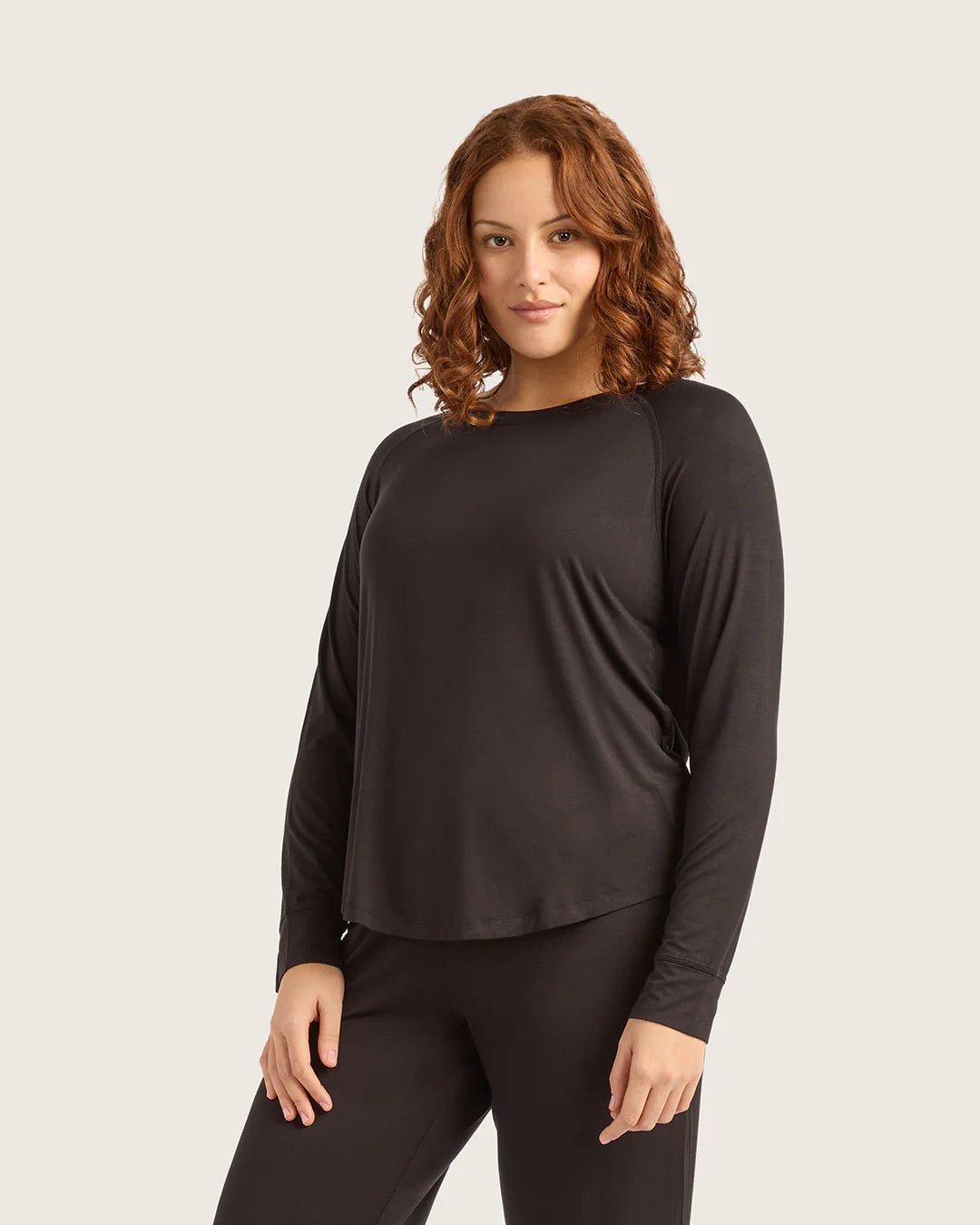 Woman wearing a black long-sleeve top and pants on a light beige background