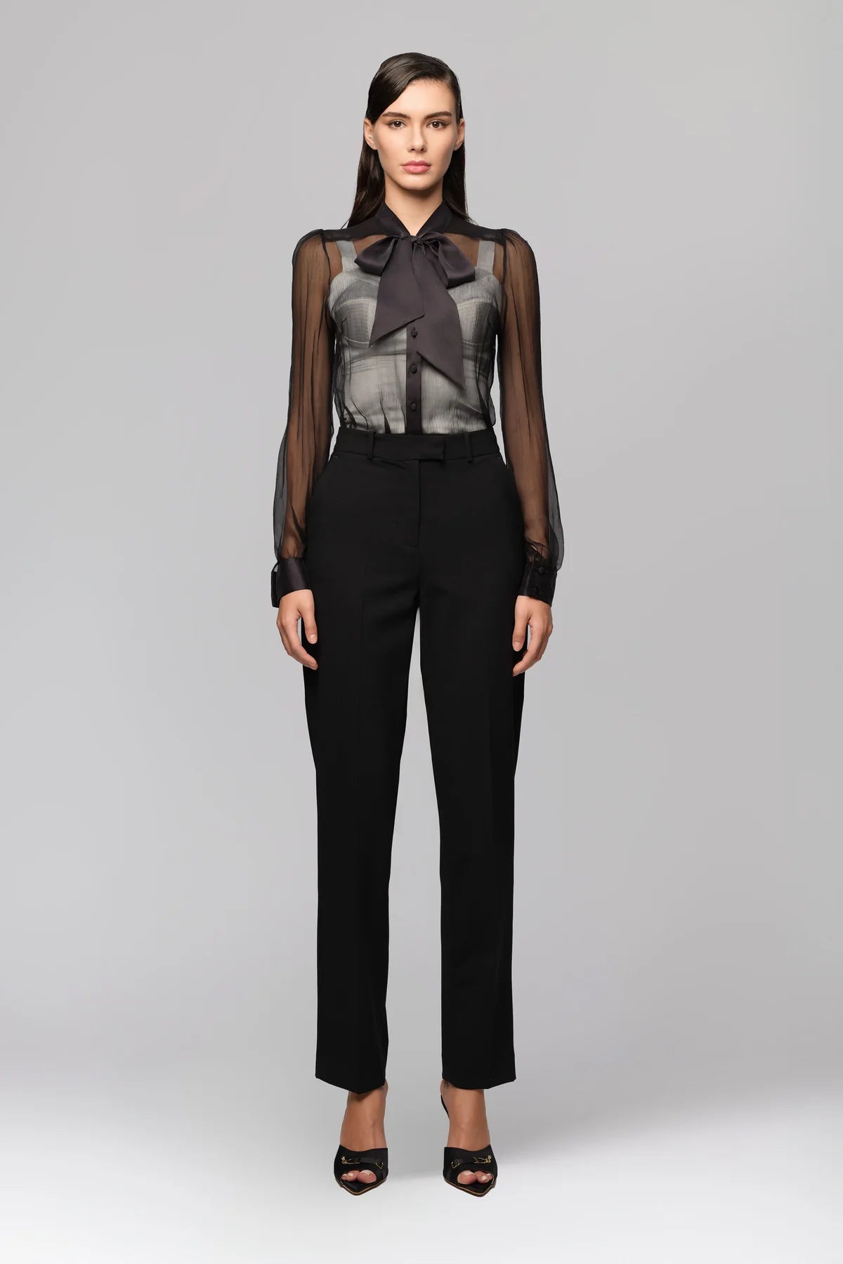 Woman wearing a black outfit with sheer top and black pants on a gray background