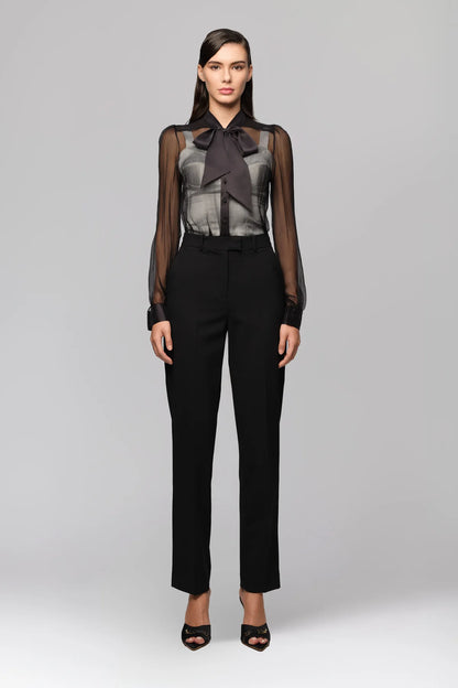 Woman wearing a black outfit with sheer top and black pants on a gray background