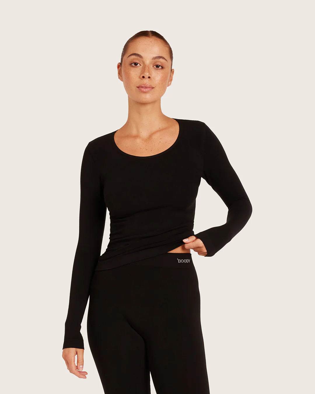 Woman wearing a black long-sleeve top and black leggings on a light gray background