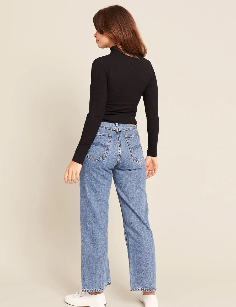 Person wearing blue jeans and a black top on a beige background