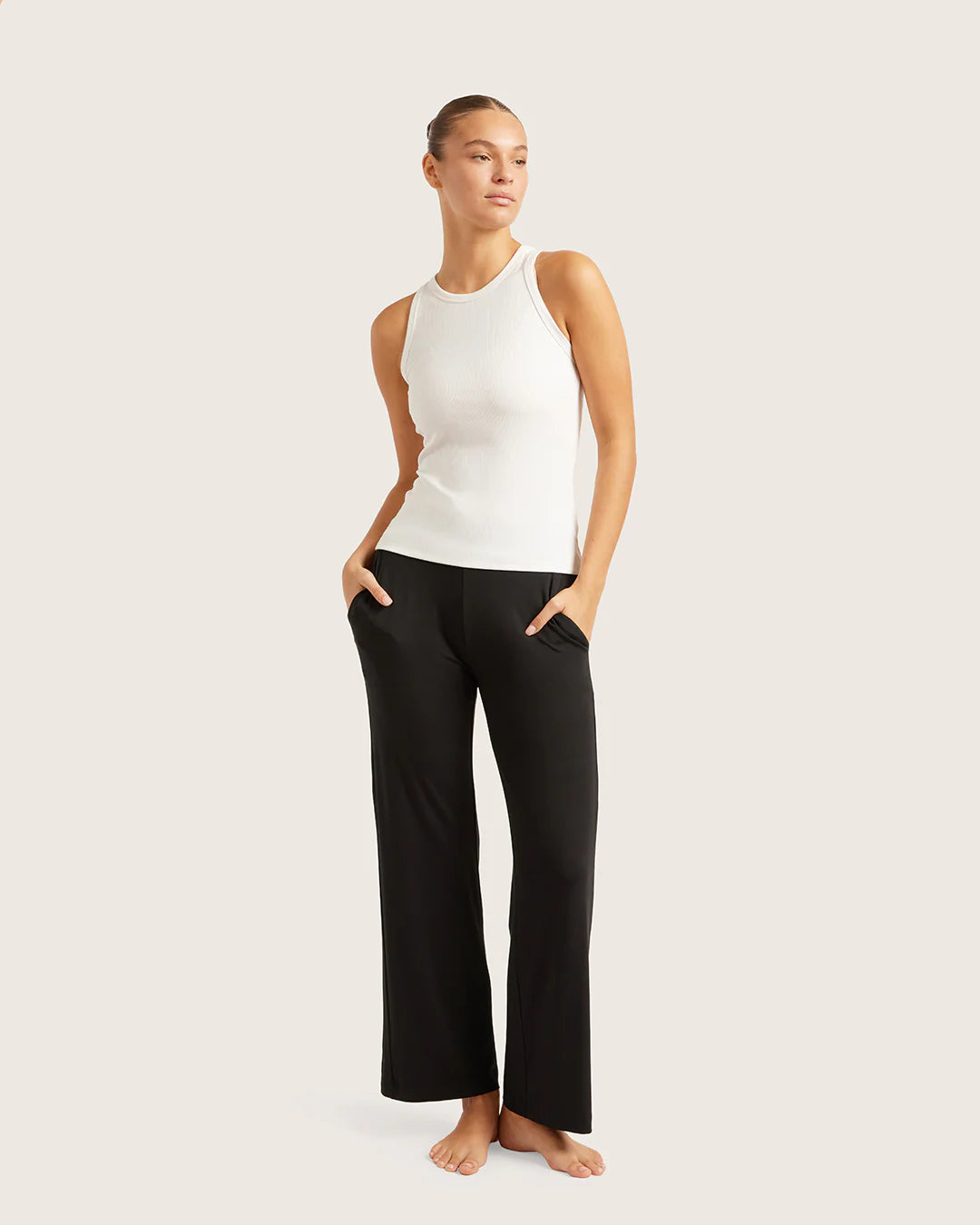 Woman wearing a white sleeveless top and black pants on a plain background
