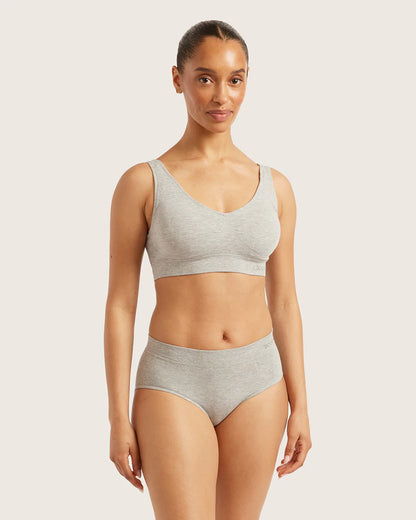 Woman wearing a gray sports bra and high-waisted underwear on a light background