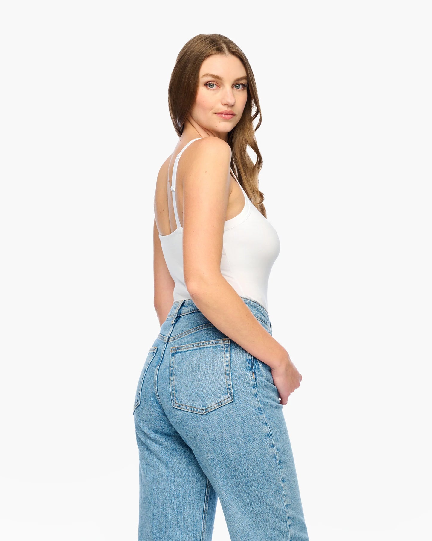 Woman wearing a white tank top and blue jeans on a white background