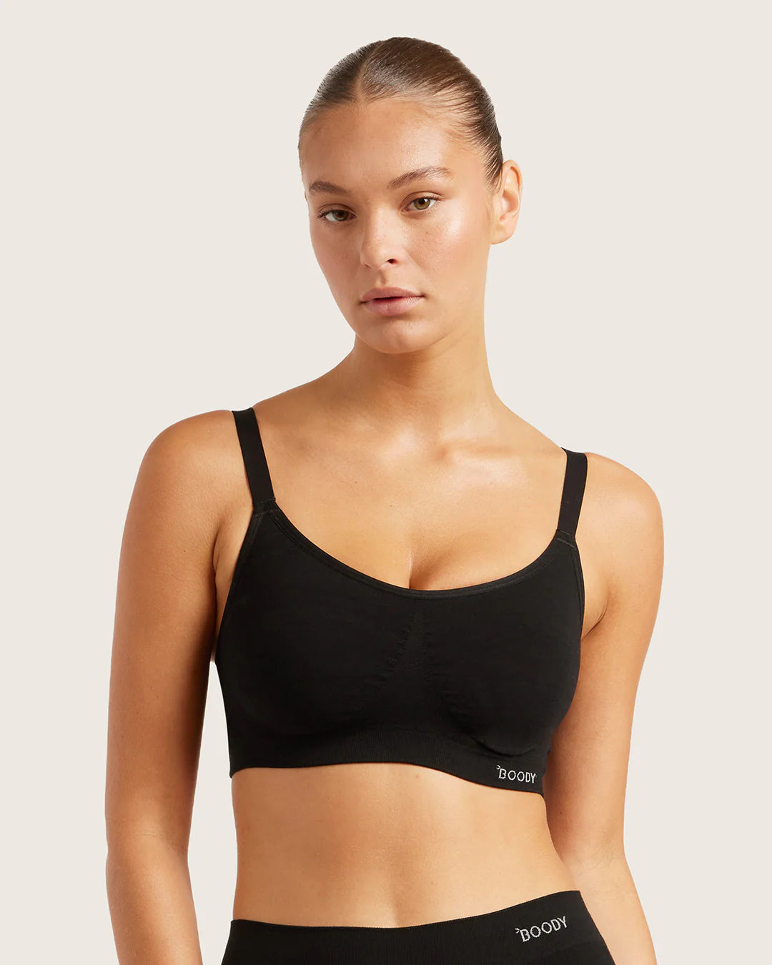 Woman wearing a black sports bra with 'hood' branding on a light background