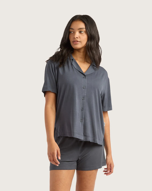 Woman wearing a gray button-up shirt and shorts on a beige background