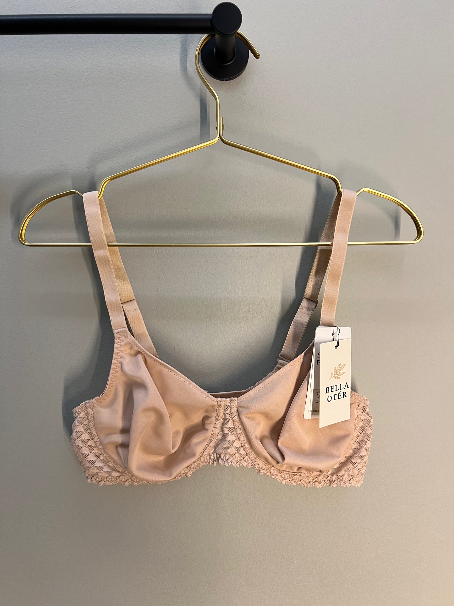 Beige bra on a gold hanger with a visible brand tag against a gray background