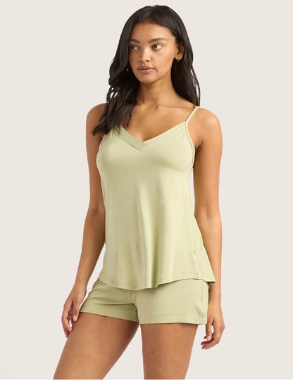Woman wearing a light green tank top and shorts on a plain background