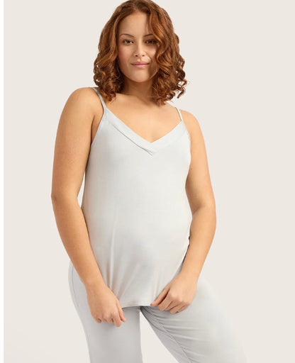 Woman wearing a white sleeveless top and pants on a plain background