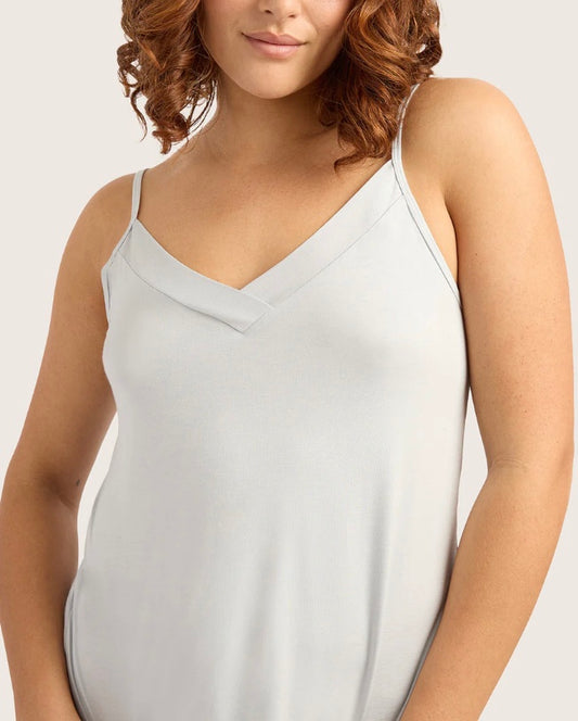 Woman wearing a light gray spaghetti strap top against a plain background