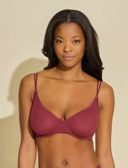 Woman wearing a maroon bra against a beige background
