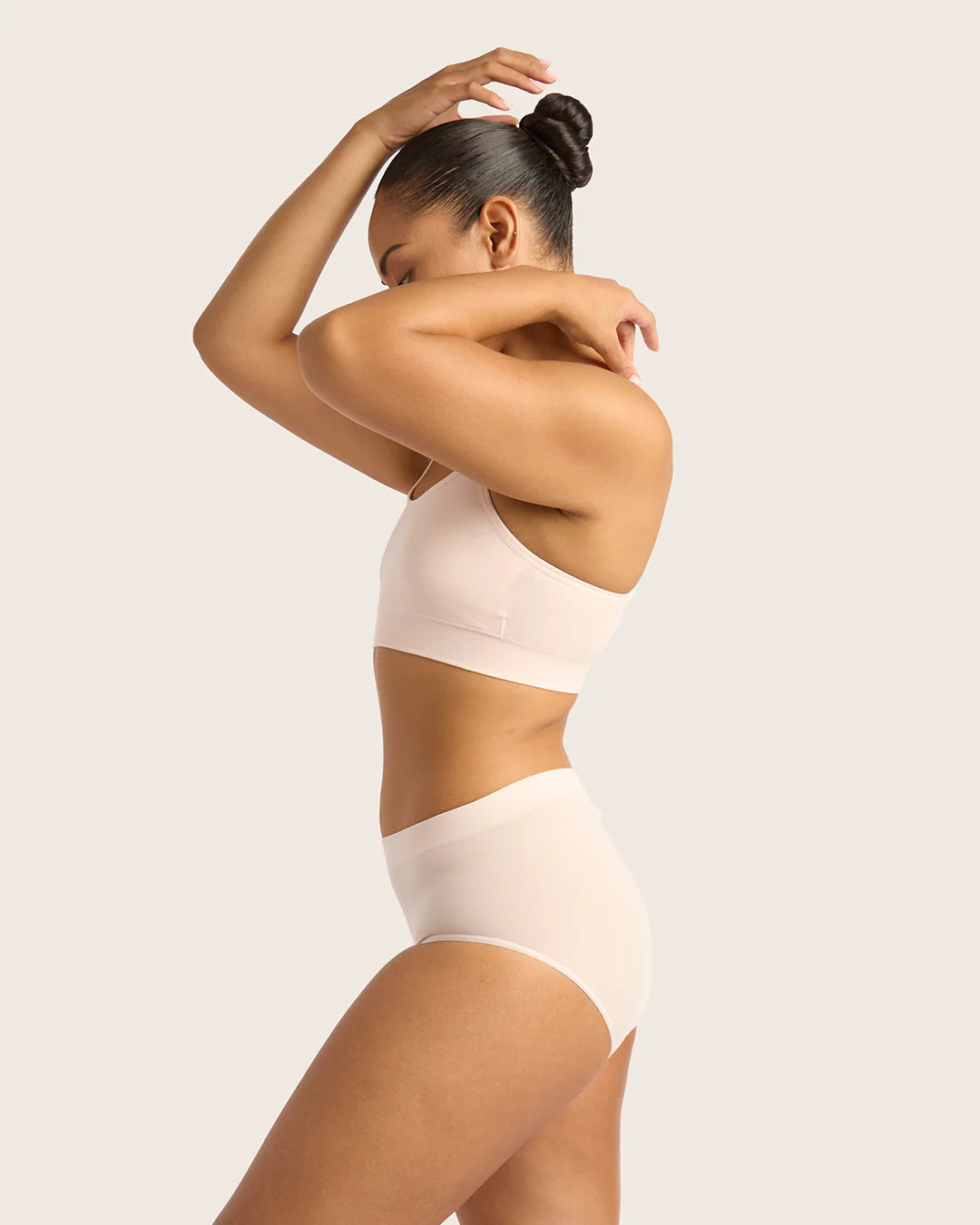 Woman wearing a beige bodysuit against a light background
