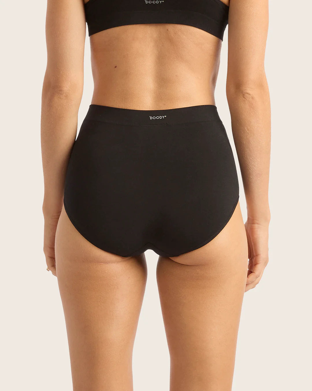 Person wearing black high-waisted underwear with 'bodysuit' branding on a light background