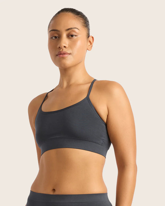 Woman wearing a dark gray sports bra and leggings on a light beige background
