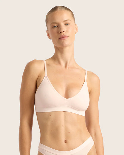 Woman wearing a light pink bra and underwear set against a plain background
