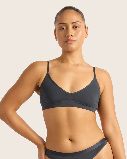Woman wearing a dark gray sports bra and underwear set on a plain background