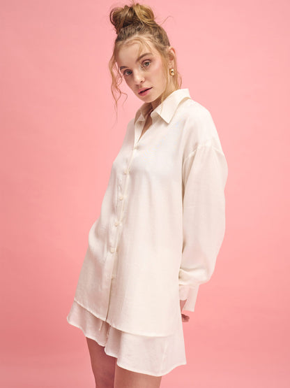 Woman wearing a white shirt dress against a pink background