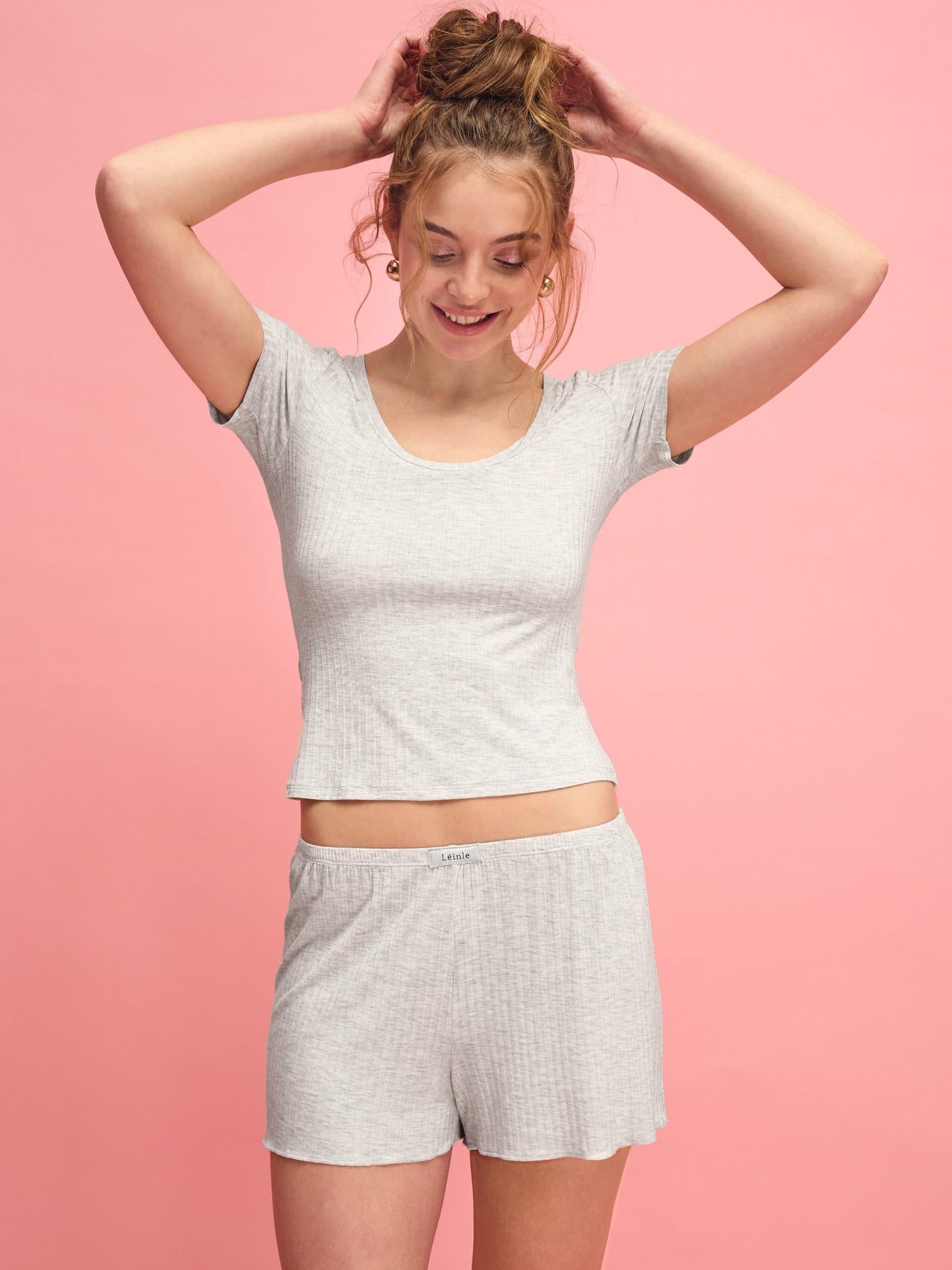 Woman wearing a gray crop top and shorts against a pink background