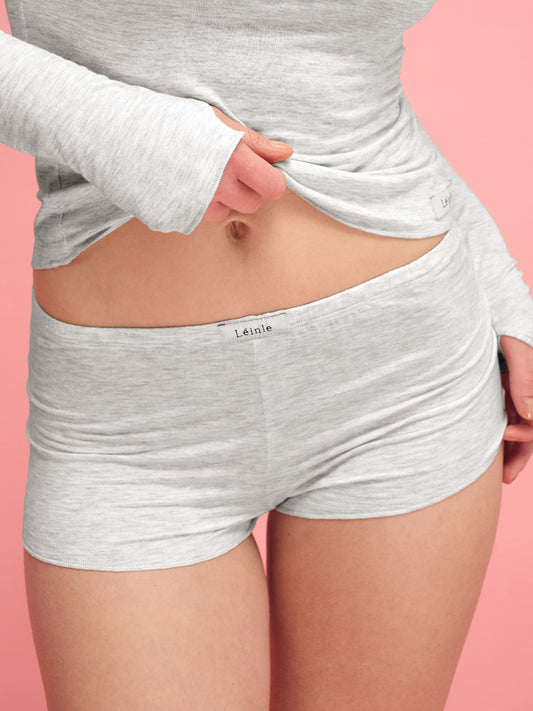 Person wearing gray shorts with a visible brand logo on a pink background