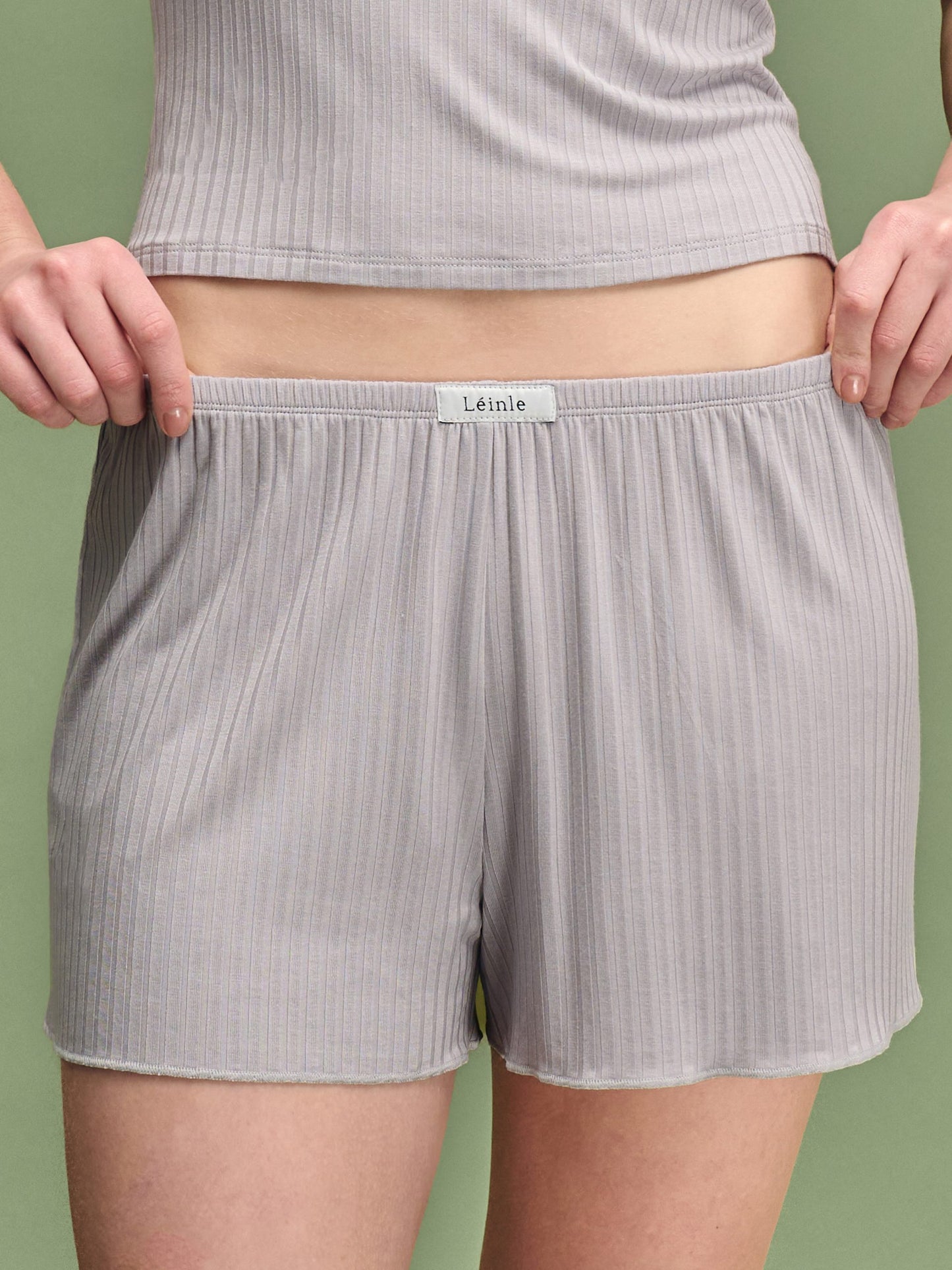 Person wearing gray ribbed shorts with a visible brand label on a green background