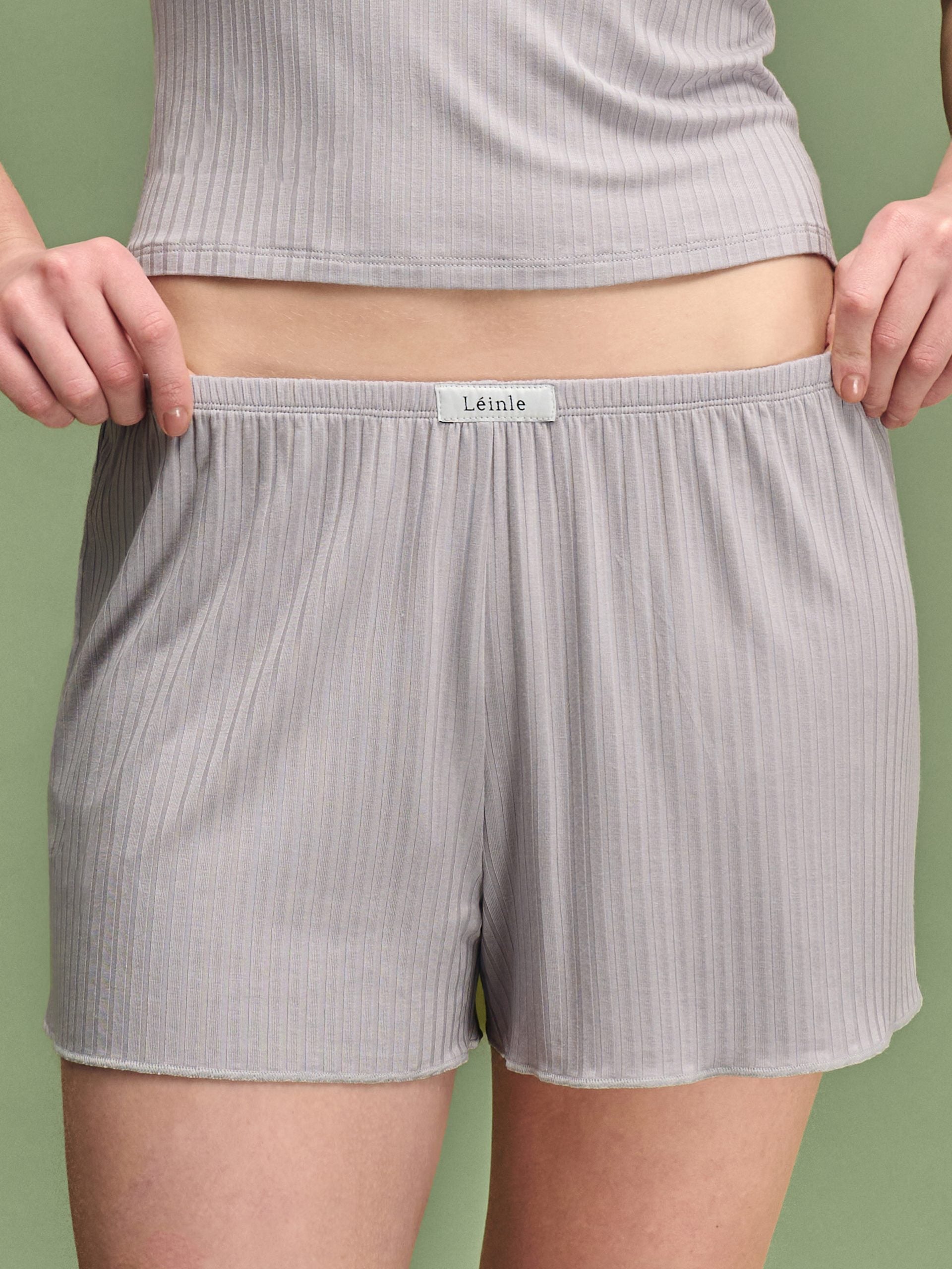 Person wearing gray ribbed shorts with a visible brand label on a green background