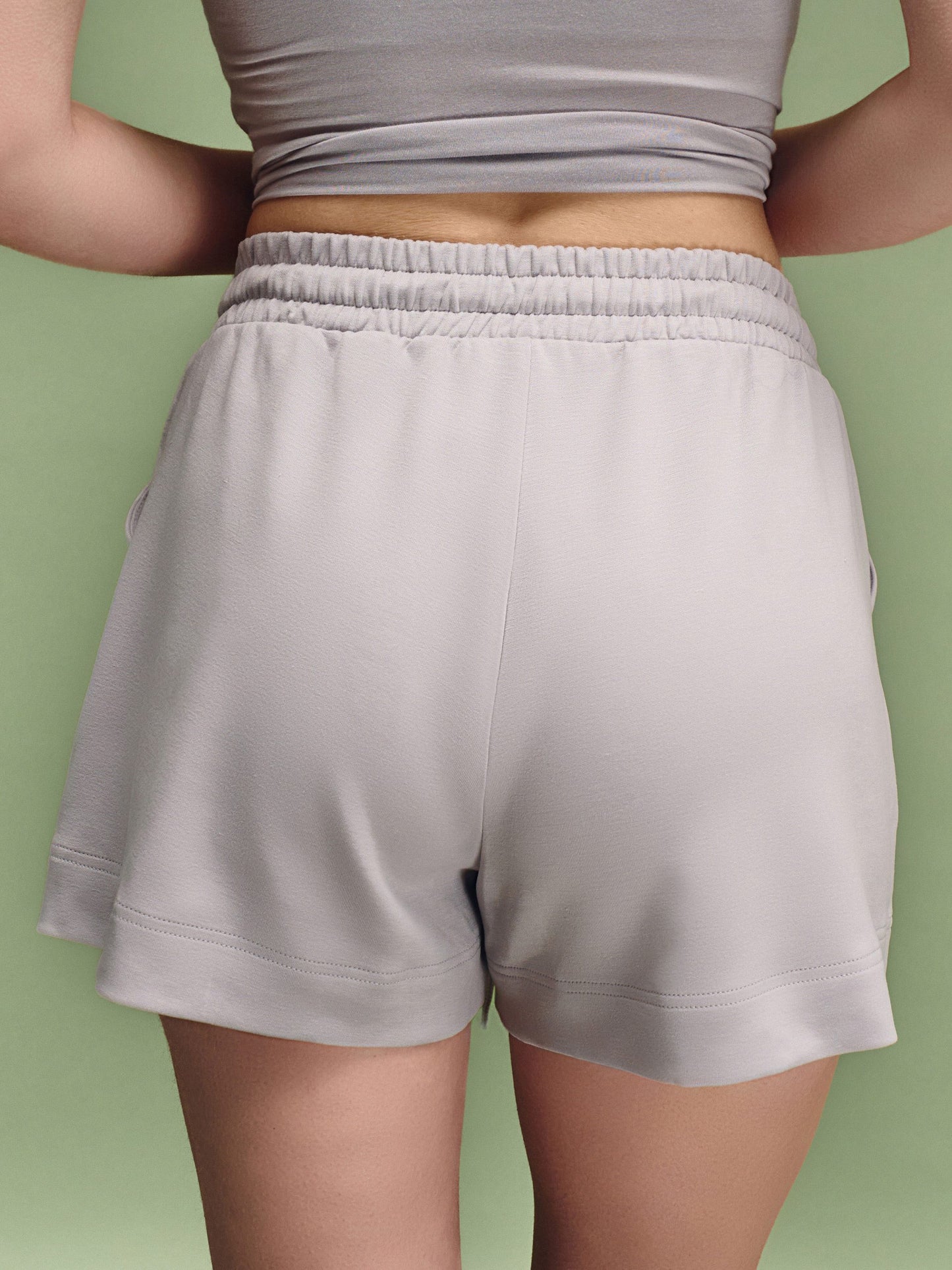 Person wearing light gray shorts and a crop top against a green background