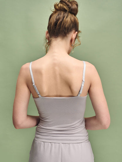 Woman wearing a light gray tank top against a green background