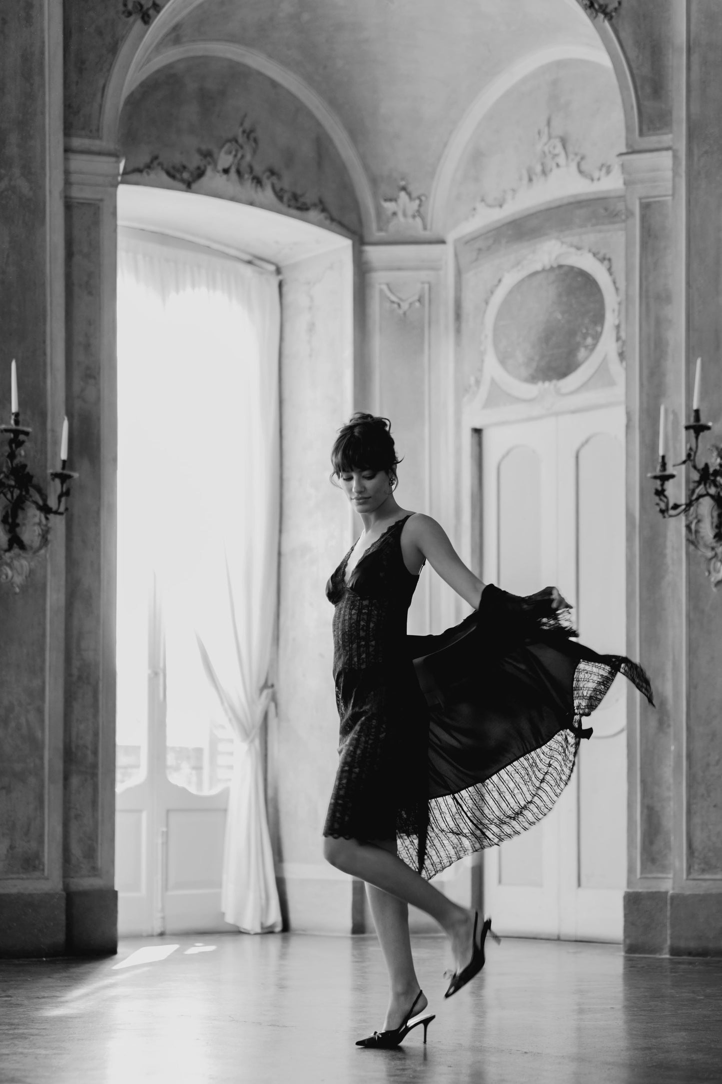 Woman in a black dress standing in an elegant room with decorative walls and candelabras.