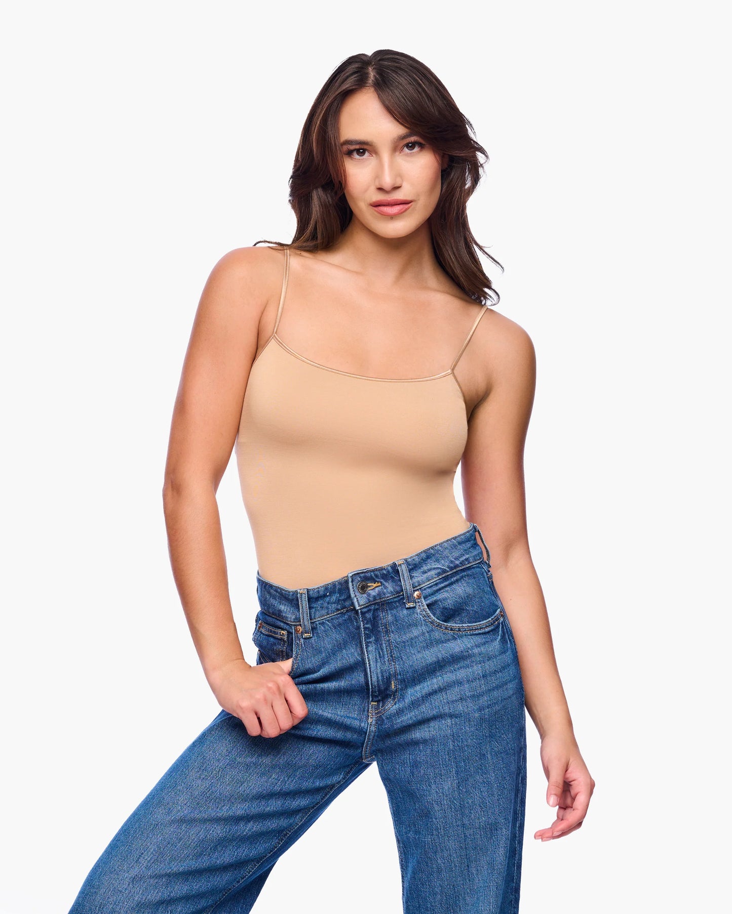 Woman wearing a beige tank top and blue jeans on a white background