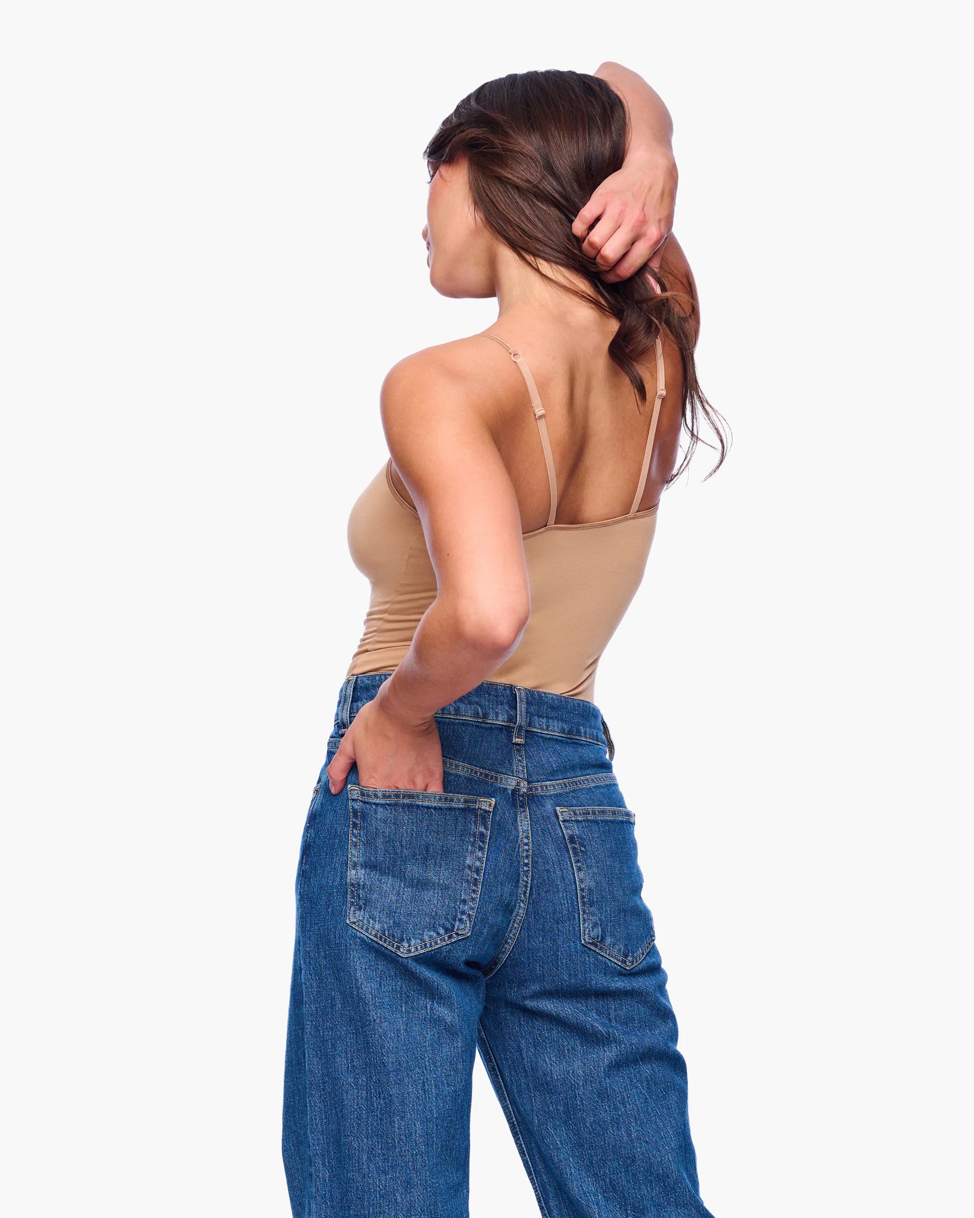 Woman wearing a beige top and blue jeans on a white background