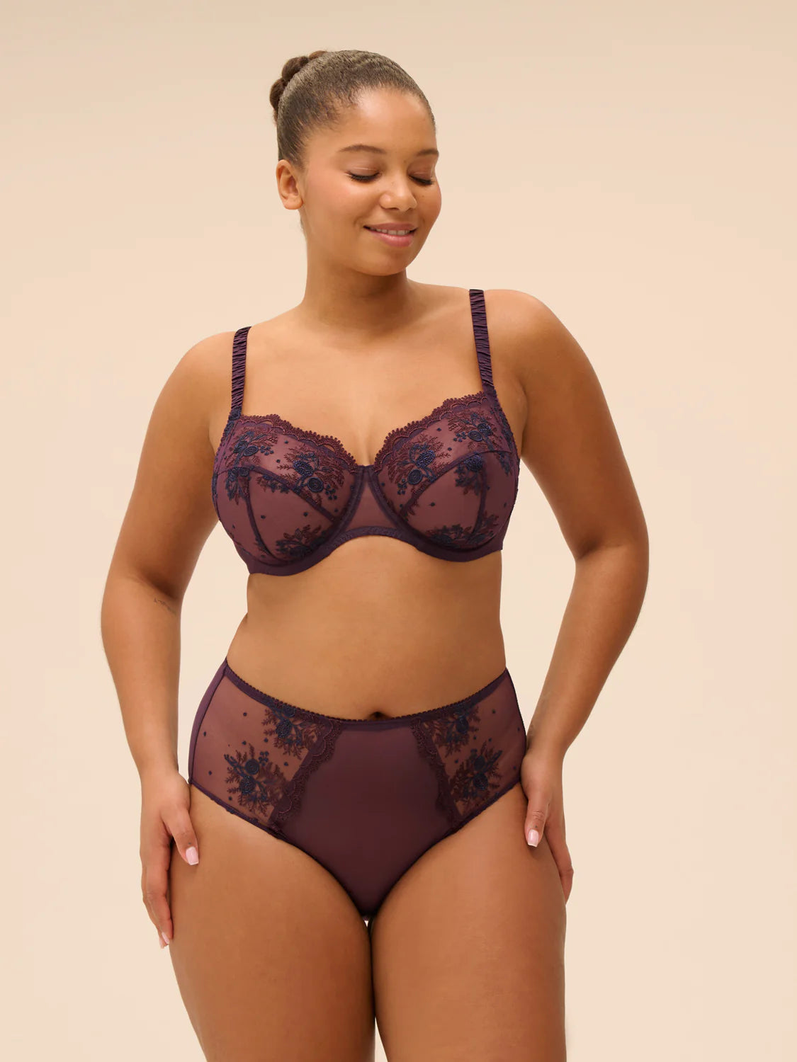 Woman wearing a dark lace lingerie set against a beige background